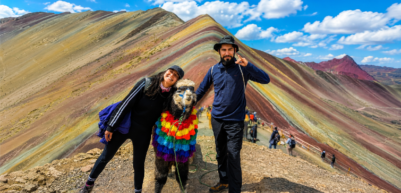 Travelers posing with a decorated alpaca at the Rainbow Mountain viewpoint in Vinicunca near Cusco, Peru.