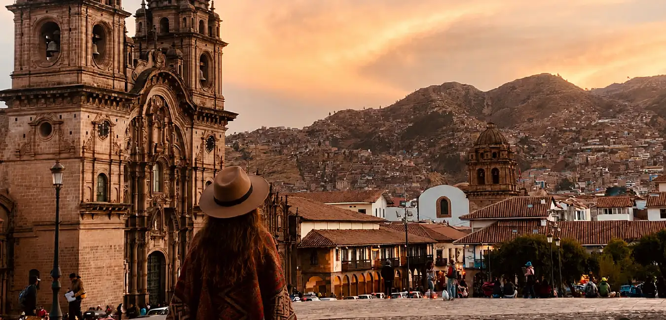 Tourist admiring the Cusco Cathedral at sunset from Plaza de Armas, with colonial architecture and the Andean mountains in the background.