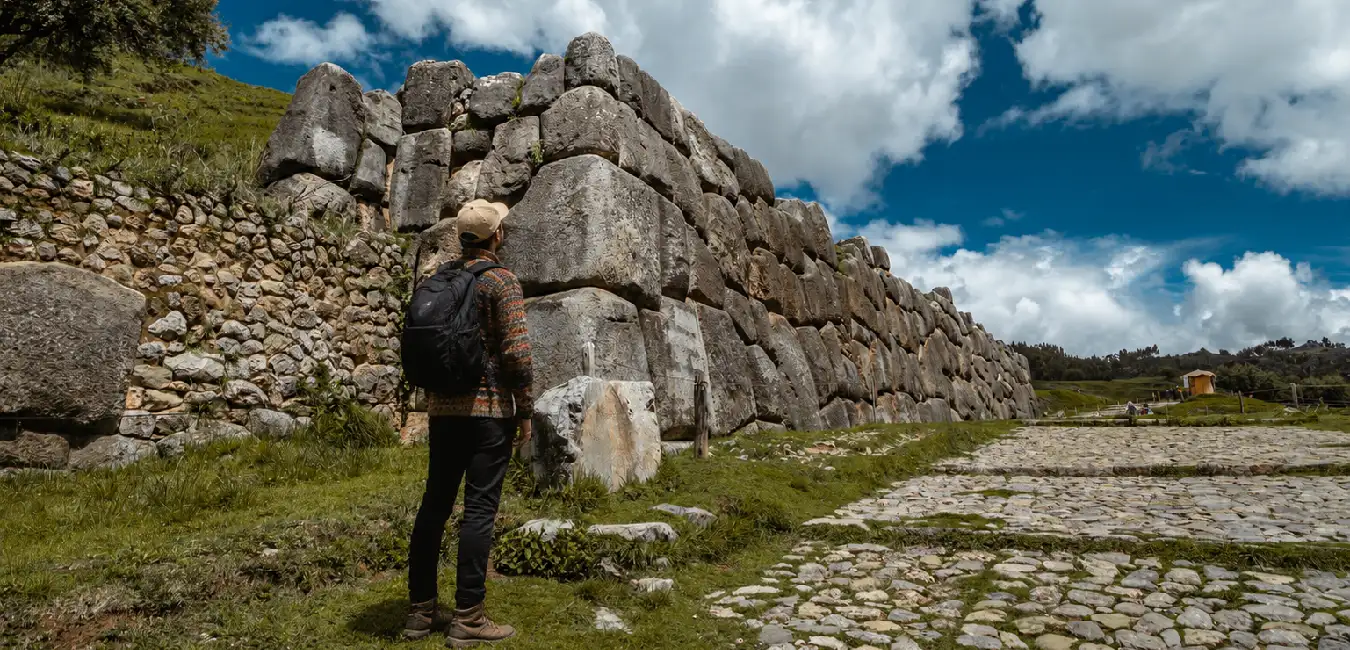 Traveler admiring the massive Inca stone walls of Sacsayhuamán under a dramatic sky in Cusco 
